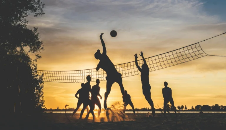 A silhouette of people playing beach volleyball at sunset.