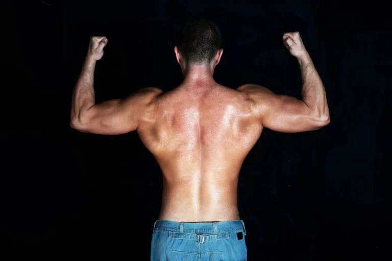 A man with an athletic, muscular build is viewed from behind against a solid black background.