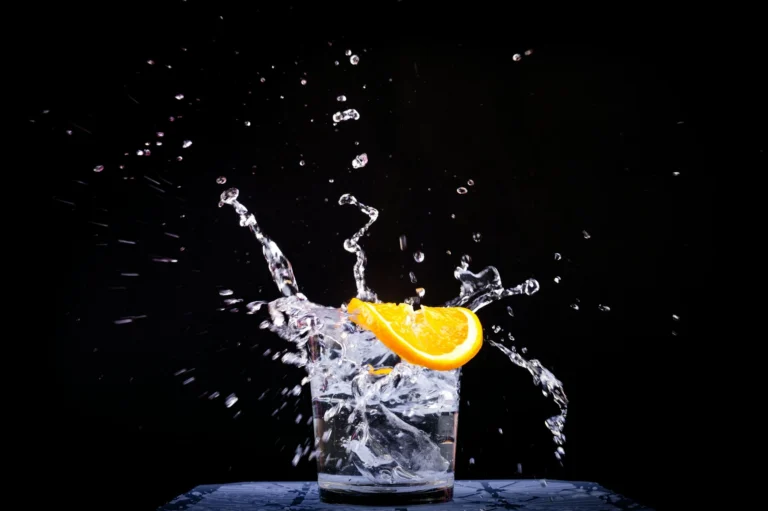 A an orange slice splashing into a clear glass of water against a black background.